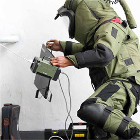 a person in a bomb-protection suit carries two devices
