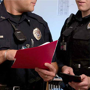 two officers speak and reference a file with papers