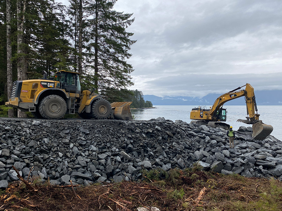 heavy construction equipment moving rock at the ocean's edge