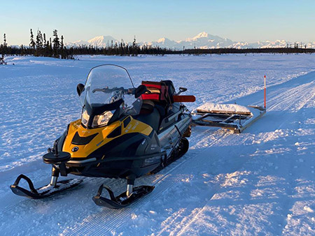 snowmachine trail grooming with mountains in the background